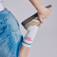 Person wearing a denim skirt and white socks with text, holding a sneaker.